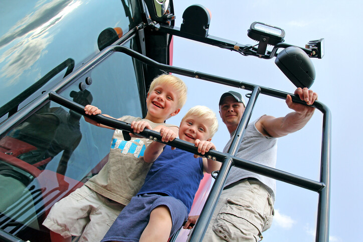 Father and two sons standing on the entrance to a large agriculture vehicle