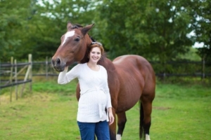 Pregnant woman smiling and petting her horse