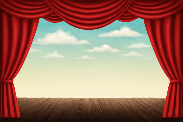 An empty stage with red curtains parted to show a blue sky