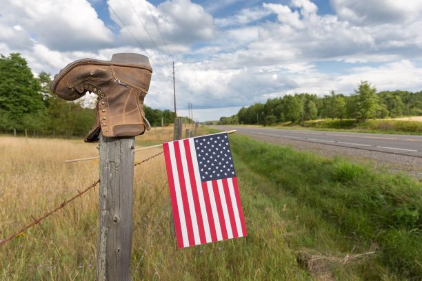 Barbwire fence post with an upside down boot and a small American flag