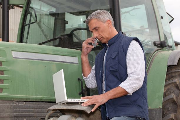 Man on cellphone and laptop beside tractor