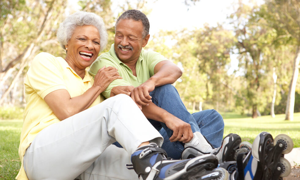 An elderly couple sitting down, laughing, wearing roller skates