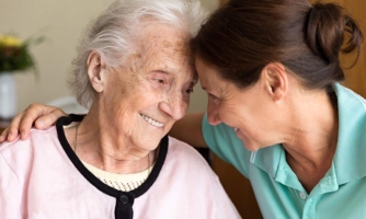 Elderly woman and nurse touching foreheads and smiling