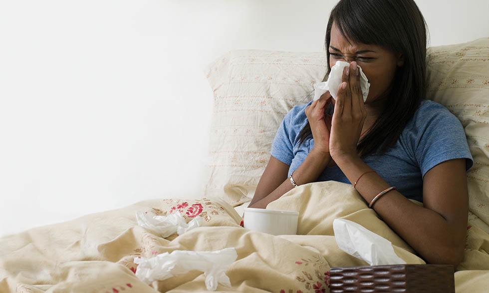Person in bed, blowing nose in tissue