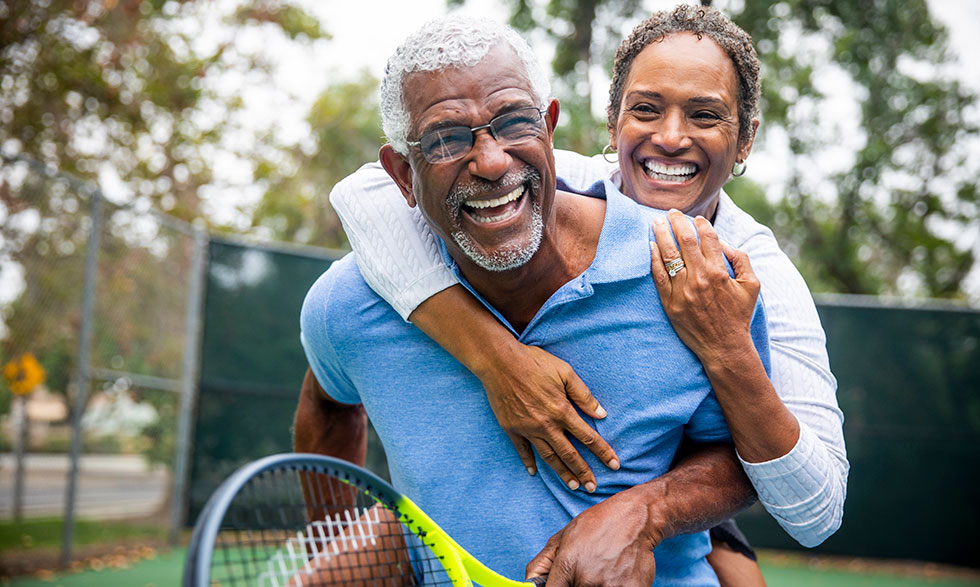Older couple hugging and smiling while they play tennis