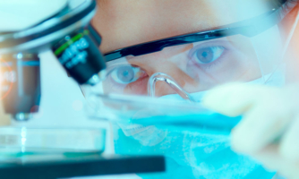 Person in lab gear looking into a microscope