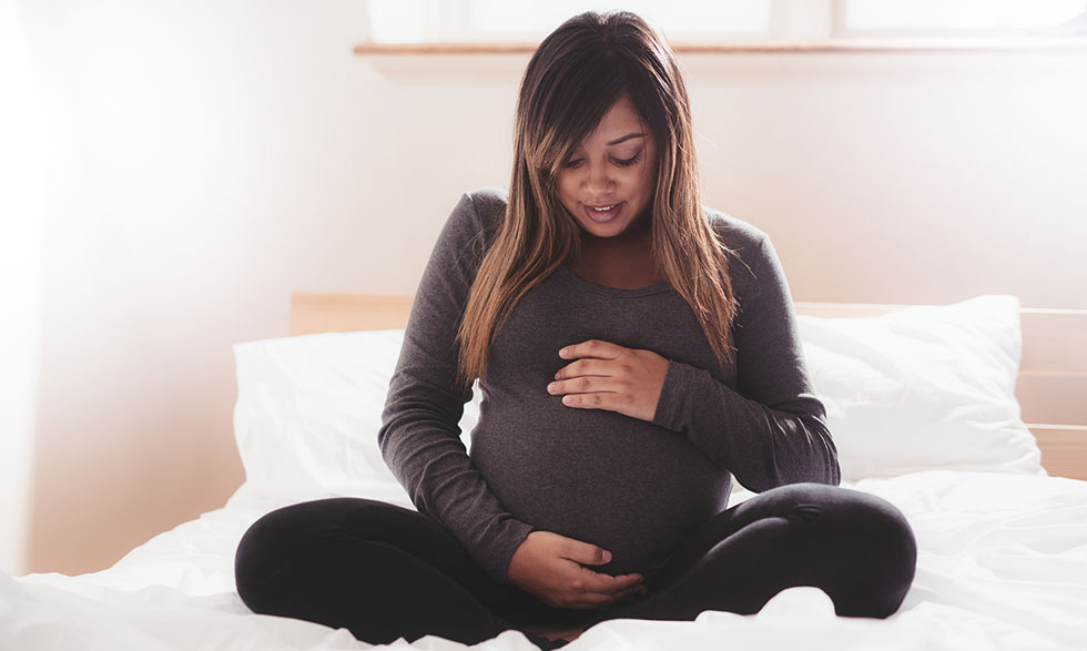Pregnant person sitting on bed, holding belly.