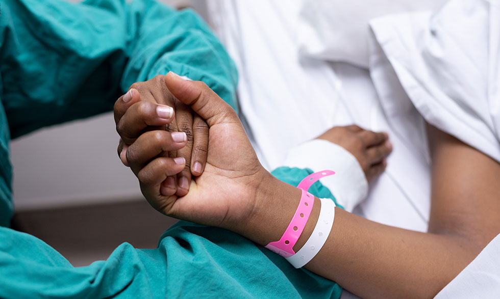 Someone in scrubs holding the hand of someone wearing a hospital bracelet.