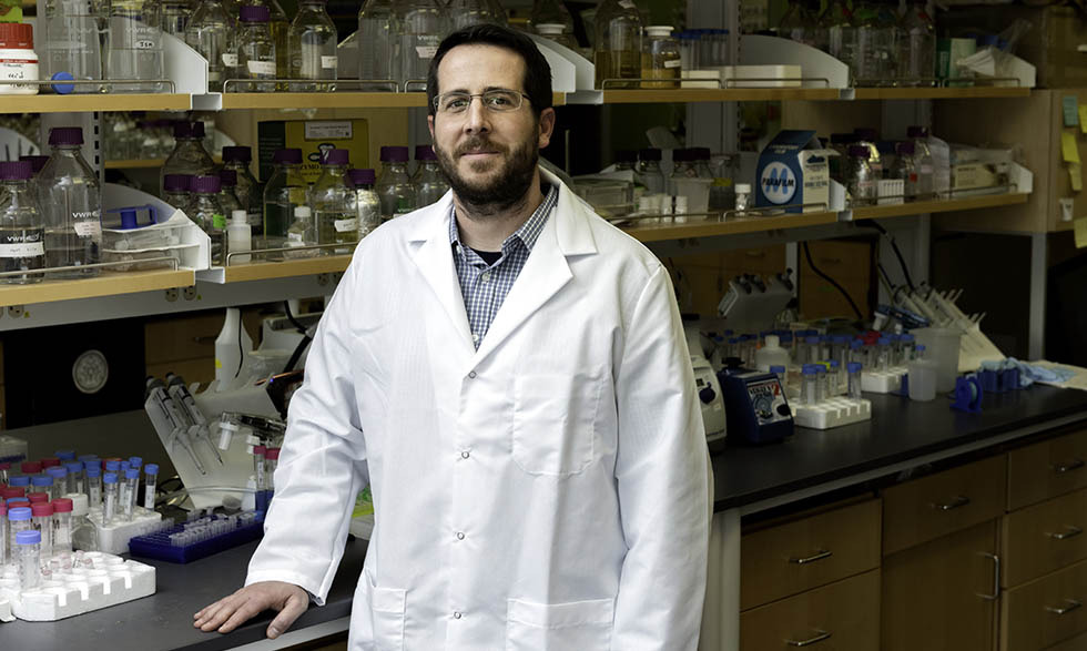 Headshot of researcher Jason McLellan, Ph.D. in lab coat in front of science equipment